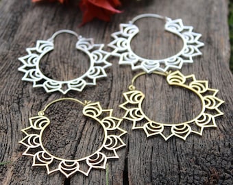 May include: Two pairs of silver and gold hoop earrings with a mandala design. The earrings are on a wooden surface.