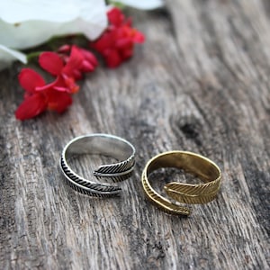 May include: Two adjustable rings with a feather design. The ring on the left is silver and the ring on the right is gold.