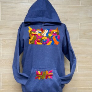 May include: A blue hooded sweatshirt with colorful embroidery on the front and a smaller design on the pocket.