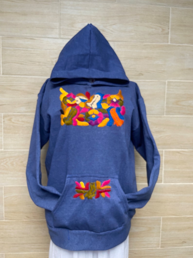 May include: A blue hooded sweatshirt with colorful embroidery on the front and a smaller design on the pocket.