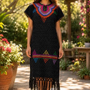 May include: Black embroidered dress with colorful floral patterns around the neckline and hem. The dress has short sleeves and a diamond pattern. The hemline is finished with fringe. The dress is knee-length.