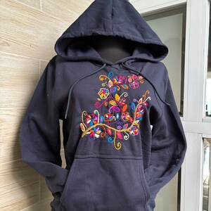 May include: A navy blue hooded sweatshirt with a colorful floral embroidery design on the front. The sweatshirt has a kangaroo pocket and a drawstring hood.