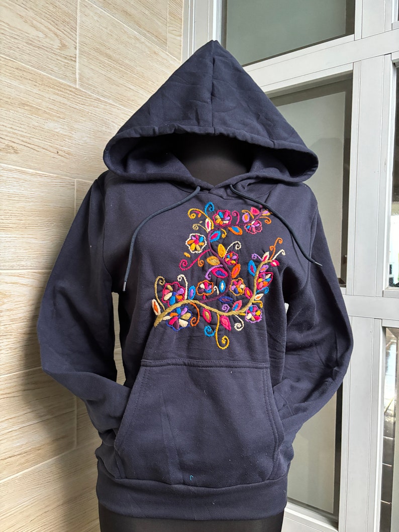 May include: A navy blue hooded sweatshirt with a colorful floral embroidery design on the front. The sweatshirt has a kangaroo pocket and a drawstring hood.