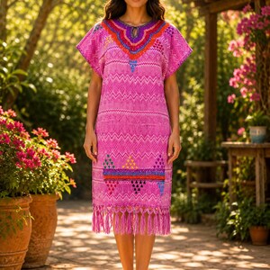 May include: A pink, knee-length dress with short sleeves and a fringed hem. The dress features colorful embroidered details around the neckline and hem, with a geometric pattern. The dress is worn outdoors in a garden setting.