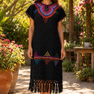 May include: Black embroidered dress with colorful floral patterns around the neckline and hem. The dress features short sleeves and a fringe hemline. The dress is knee-length and has a diamond pattern throughout the fabric.