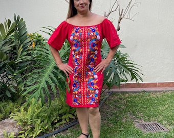 May include: A red off-the-shoulder dress with vibrant floral embroidery. The dress features a knee-length hemline and short sleeves. The embroidery includes blue, yellow, and red flowers. The person is wearing black sandals.