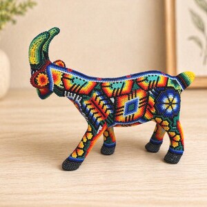 May include: A colorful beaded goat figurine. The goat is decorated with intricate patterns in shades of blue, orange, yellow, green, and black. The figurine has curved horns and is standing on four legs.