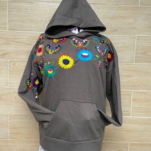 May include: A gray hooded sweatshirt with colorful embroidered flowers on the front. The sweatshirt has a kangaroo pocket.