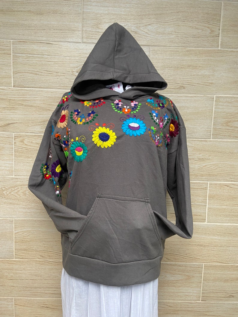 May include: A gray hooded sweatshirt with colorful embroidered flowers on the front. The sweatshirt has a kangaroo pocket.