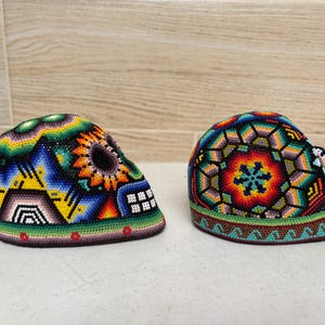 以下が含まれることがあります： カラフルなビーズで作られた2つのスカル型の装飾品。青、黄、緑、赤など、さまざまな色で複雑な模様が施されています。デザインは幾何学模様と花柄を特徴とし、詳細な職人技を示しています。