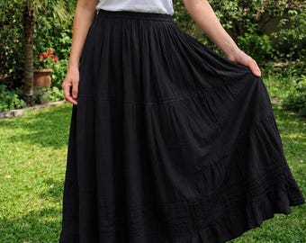 May include: A white sleeveless tank top with a scoop neckline paired with a long, black, tiered maxi skirt. The skirt features a gathered elastic waistband, multiple horizontal stitched panels, and a ruffled hemline that reaches the ankles.