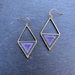Könnte beinhalten: Ein Paar goldene Dreiecksohrringe mit violetten und blauen Perlenmustern.