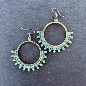 May include: A pair of silver hoop earrings with turquoise and gold beads. The earrings are beaded in a graduated pattern with the turquoise beads getting larger as they go down the hoop.