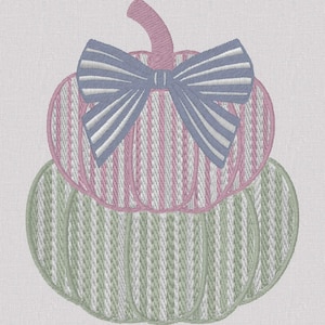 May include: An embroidery design featuring two stacked pumpkins. The top pumpkin is pink with white vertical stripes and a blue and white striped bow. The bottom pumpkin is light green with white vertical stripes. The design is on a white fabric.