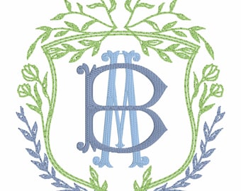 Op de afbeelding: Geborduurd monogramontwerp met de letters B en M in licht- en middenblauw, geplaatst in een schildvormige lijst. De lijst is versierd met groene en blauwe bloemelementen, waardoor een decoratief en elegant embleem ontstaat.