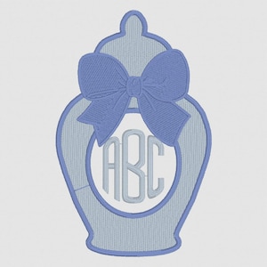 May include: A light blue embroidered design of a decorative jar with a bow and the letters "ABC" inside a circle. The jar has a textured appearance and is set against a white background. The bow is a darker shade of blue.