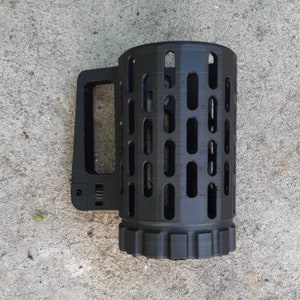 May include: Black mug with a distinctive, cage-like design. It has a rectangular handle and a cylindrical body with many vertical and horizontal openings. The base has a ridged pattern. The mug is made of a matte black material.