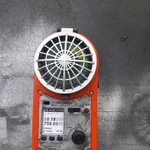 Puede incluir: Dispositivo electrónico naranja y plateado con una rejilla circular en la parte superior. El dispositivo tiene una pantalla digital que muestra lecturas y una perilla. El texto "ВЕДМІДЬ" es visible.