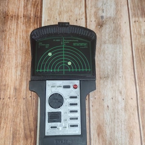 May include: A black and grey prop radar device with a green screen showing radar graphics. The device has buttons and a handle. The text "21.10.01" and "Parametricheskij andis" are visible on the screen.