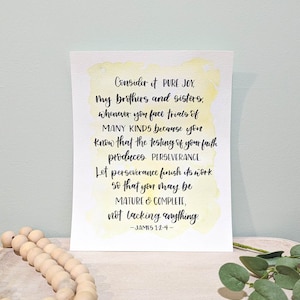 May include: A watercolor print with a yellow background and black text. The text reads "Consider it PURE JOY, my brothers and sisters, whenever you face trials of MANY KINDS because you know that the testing of your faith produces PERSEVERANCE. Let perseverance finish its work so that you may be MATURE & COMPLETE, not lacking anything. -JAMES 1:2-4- "