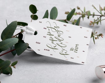 May include: White gift tag with the text "Happy Holidays" in green cursive script. The tag has a brown string attached and is decorated with small brown and pink tree illustrations.