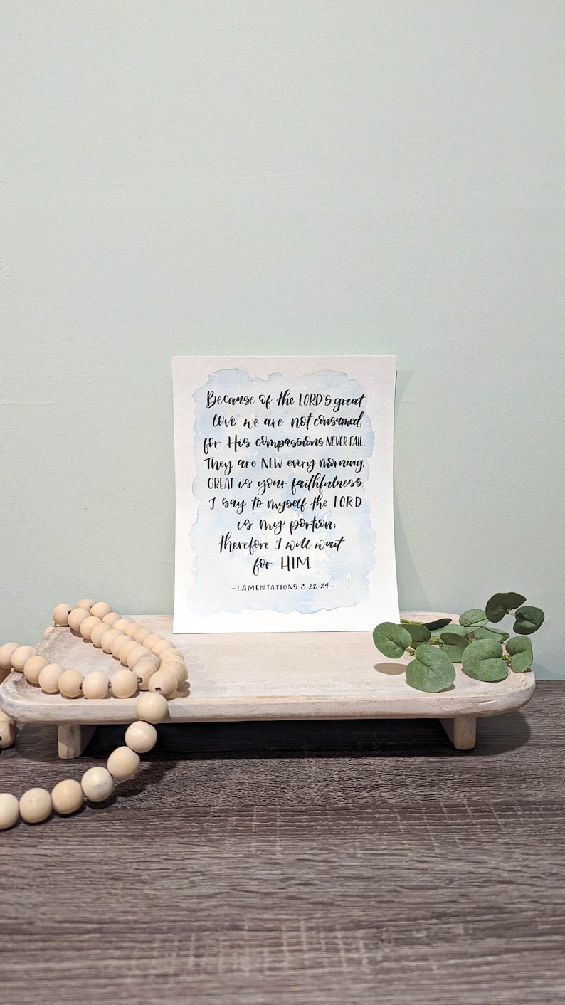 May include: A watercolor print with a blue and white background featuring a bible verse from Lamentations 3:22-24. The verse reads "Because of the LORD'S great love we are not consumed, for His compassions never fail. They are new every morning. Great is your faithfulness. I say to myself, the LORD is my portion. Therefore I will wait for HIM."