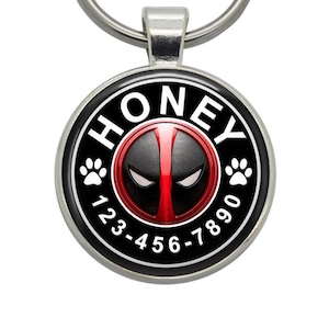 May include: A black and red round dog tag with the word "HONEY" in white letters around the edge. A red and black Deadpool mask is in the center of the tag. The tag also has two white paw prints and the phone number 123-456-7890.
