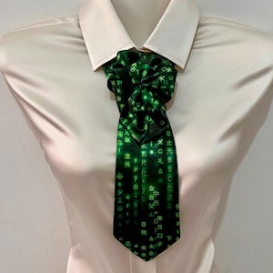 May include: A cream-colored button-down shirt featuring a necktie with a black background and a digital green pattern of falling characters, symbols, and letters. The tie is tied in a gathered knot style, resting against the collar of the shirt.