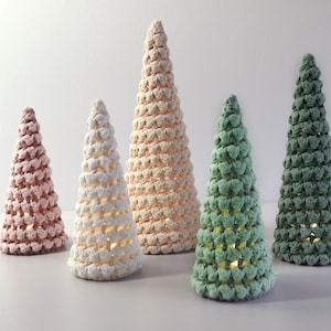 Może przedstawiać: Pięć szydełkowych ozdób choinkowych w różnych rozmiarach. Drzewka wykonane są z włóczki w odcieniach różowego, białego i zielonego.