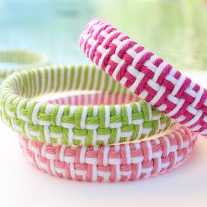 May include: Three woven bracelets in pink, green, and white. The bracelets are stacked on top of each other.