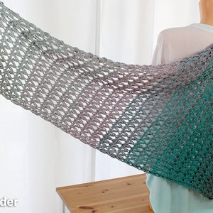 Può includere: Uno scialle all'uncinetto con un gradiente di colori verde, blu e viola. Lo scialle è realizzato con un delicato punto traforato.