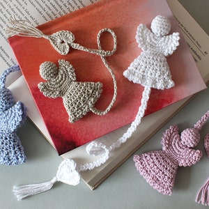 Könnte beinhalten: Vier gehäkelte Engels-Lesezeichen mit Herz- und Quasten-Akzenten. Die Engel sind in Weiß, Hellblau, Beige und Rosa.