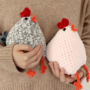 Puede incluir: Dos pollos de peluche tejidos a crochet, uno gris y blanco, el otro rosa. Ambos tienen crestas de fieltro rojo y picos y patas de fieltro naranja.