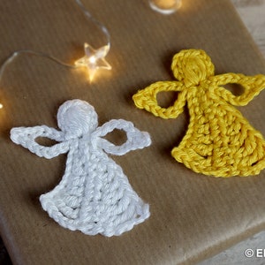 May include: Two crocheted angels, one white and one yellow, on a brown background. The angels are made with yarn and have a simple design.