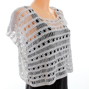 Puede incluir: Un top blanco de ganchillo con un delicado patrón de calado. El top tiene mangas cortas y un escote redondo.