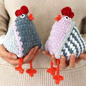 Puede incluir: Dos pollos de peluche tejidos a crochet, uno gris y otro rosa, con detalles blancos y grises. Ambos pollos tienen crestas rojas y patas naranjas.