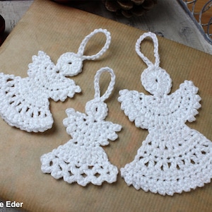 以下が含まれることがあります： 吊るすためのループが付いた、白のクロシェ編み天使のオーナメント3つ。天使は繊細なレース編みのステッチで作られています。