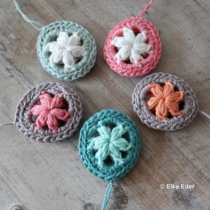 May include: Five crocheted round ornaments with a star design in the center. The ornaments are in shades of pink, peach, teal, green, and white.