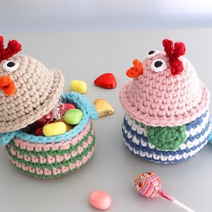 May include: Two crocheted chick baskets with colorful striped patterns. The baskets are open and filled with colorful candies. One basket is beige with a red comb and the other is pink with a green wing.