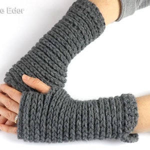 以下が含まれることがあります： ニット糸で編まれたグレーの指なし手袋のペア。手袋は人の手に着用されています。
