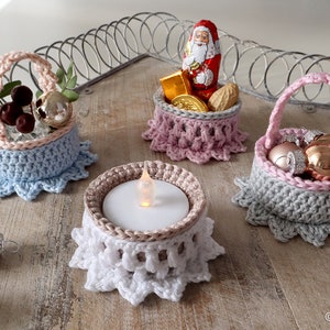 Könnte beinhalten: Vier gehäkelte Körbe mit verschiedenen farbigen Besätzen und Dekorationen. Die Körbe sind gefüllt mit kleinen Weihnachtskugeln, einem Schokoladen-Weihnachtsmann und einem Teelicht.