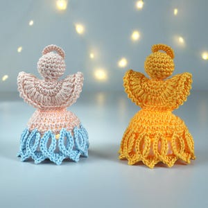 以下が含まれることがあります： 手作りのかぎ針編み天使の置物2つ。1つはピンクと青、もう1つは黄色です。どちらもハローと翼が広がっています。天使は、クリスマスやお祝いなどの装飾品である可能性があります。