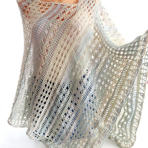 Könnte beinhalten: Ein gehäkeltes Poncho in Creme-, Blau- und Grüntönen. Das Poncho hat ein zartes Lochmuster und einen gewellten Rand.