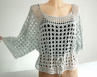 Peut inclure: Un haut en crochet bleu clair avec un motif ajouré et ample. Le haut a une encolure arrondie, des manches trois-quarts et une taille à cordon. Le vêtement est présenté sur un mannequin.
