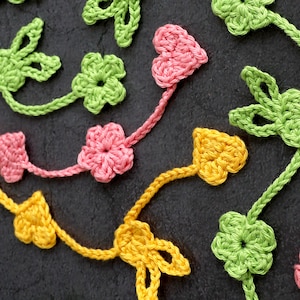 Könnte beinhalten: Eine gehäkelte Girlande mit grünen Blättern und rosa und gelben Blüten. Die Girlande ist aus Garn gefertigt und eignet sich perfekt zum Dekorieren eines Hauses oder einer Party.