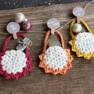 May include: Three crocheted bags with star-shaped designs in red, orange, and yellow. Each bag has a small gift inside and is hung with a clothespin and a number tag. The numbers are 2, 8, and 22.