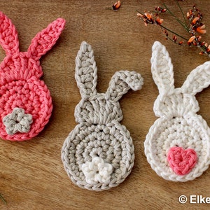 May include: Three crocheted bunny shapes, one pink, one grey, and one white, with a heart-shaped detail on each.