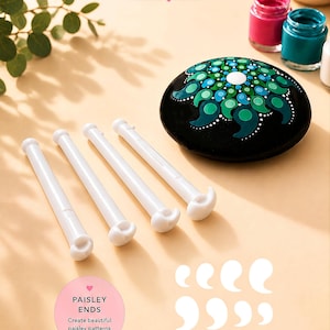 May include: Four white double-ended dotting tools with paisley-shaped tips, accompanied by a black stone painted with a green and blue mandala pattern. Text on the image reads DOUBLE ENDED and PAISLEY ENDS Create beautiful paisley patterns & swirls.