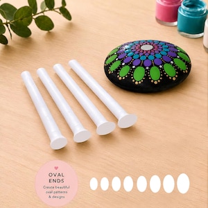May include: Four white double-ended dotting tools with flat oval tips, accompanied by a black stone painted with a colorful mandala pattern in green, blue, and purple. The text DOUBLE ENDED and OVAL ENDS Create beautiful oval patterns & designs is visible.