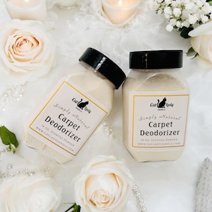 May include: Two jars of Simply Natural Carpet Deodorizer, each containing 16 oz of scented powder. The jars have black lids and labels with a cat logo and the website address. The background features white roses and candles.